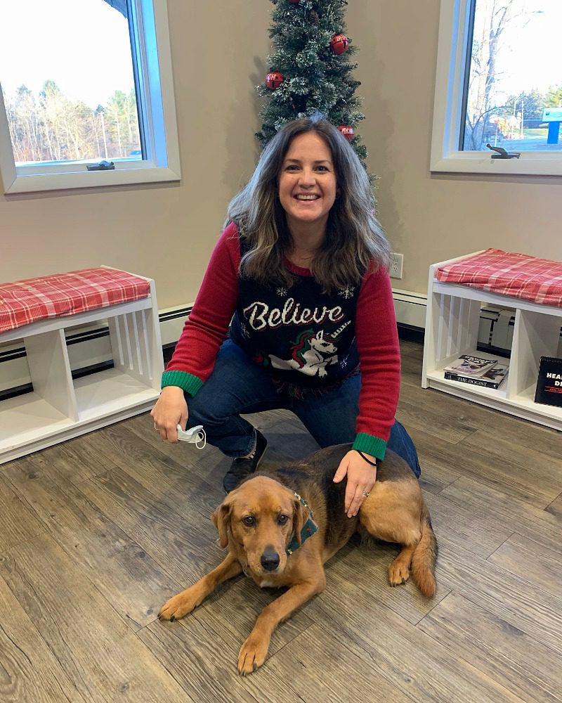 female wearing a Christmas sweater kneeling down by a big dog named Mabel